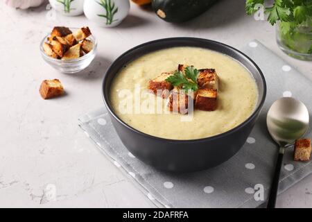 Zuppa cremosa di pollo e zucchine, servita con crostini bianchi in ciotola scura su sfondo grigio. Primo piano Foto Stock