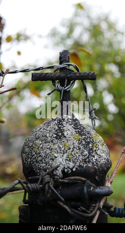 Cancello giardino che assomiglia a un memoriale per l'olocausto o la prigione con una croce d'acciaio, un filo spinato e una natura verde sfocata sullo sfondo come un simbolo di libertà Foto Stock