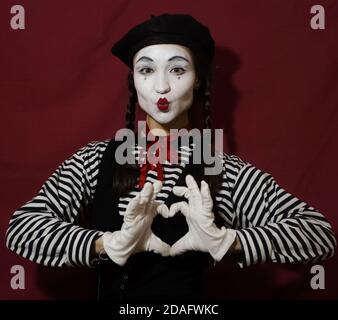 Bella ragazza mime sorride e fa un gesto di un cuore battente con le mani guardando la fotocamera. Bella ragazza nell'immagine di un mime piega a. Foto Stock