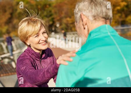 Felice coppia anziana sportiva che si allenano all'aperto. Donna matura che sorride all'uomo, toccandola le spalle mentre discute qualcosa Foto Stock