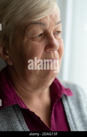 Volto di una donna anziana che guarda fuori dalla finestra. Primo piano ritratto di vecchia triste donna. Foto Stock