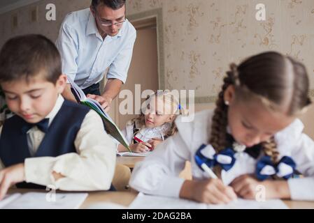 un insegnante a scuola insegna ai bambini, legge attentamente un libro. Gli studenti scrivono in un notebook. Foto Stock