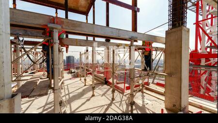 alto edificio in costruzione con lavoratori nel cantiere su supporti con uniforme di sicurezza Foto Stock