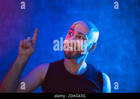 Uomo a testa calva con punti di trucco. Vernice fluorescente in luce al neon. Foto Stock