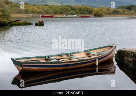 Piccola barca a remi da pesca o canoa sul lago calmo contro le barche da pesca ormeggiate a Lough Leane nel Parco Nazionale di Killarney, Contea di Kerry, Irlanda Foto Stock