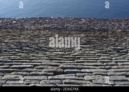 Guardando verso il basso una parete di pietra del serbatoio inclinata, si forma un'immagine di texture astratta a telaio intero. Le increspature blu profonde formano un buon spazio di copia. Foto Stock