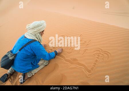 Merzouga, Marocco - APRILE 29 2019: Tradizionalmente blu vestito marocchino disegnare nella sabbia del deserto del Sahara Foto Stock