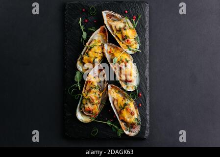 cozze al forno con formaggio e verdure su sfondo nero Foto Stock