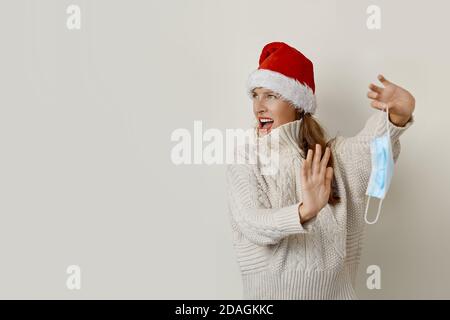 Donna che indossa un cappello Santa rimuovendo la maschera protettiva Foto Stock