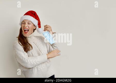 Donna che indossa un cappello Santa rimuovendo la maschera protettiva Foto Stock