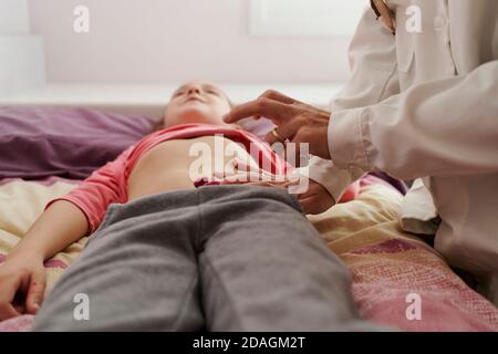 Dottore femmina che esamina l'addome di una bambina nella sua stanza. Concetto medico domestico Foto Stock