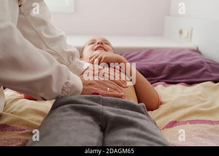 Dottore femmina che esamina l'addome di una bambina nella sua stanza. Concetto medico domestico Foto Stock