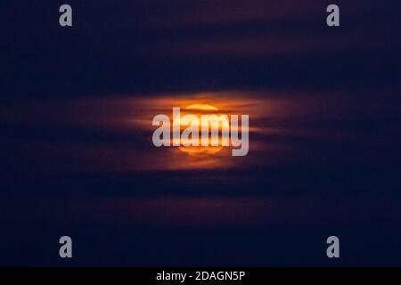 enorme luna piena di colore arancione che si respira attraverso nubi nebbie che illuminano il cielo notturno intorno ad esso, creando un'atmosfera mistica spaventosa. Luna super. Foto Stock