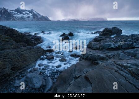 Aspre montagne di Flakstadøy si innalzano attraverso il mare dalla costa rocciosa a Vareid, Isole Lofoten, Norvegia Foto Stock