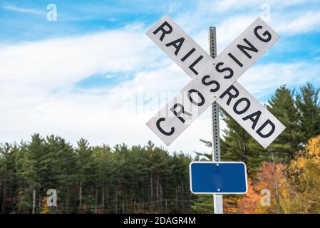 Segnale di attraversamento ferroviario con alberi e cielo nuvoloso sullo sfondo. Spazio di copia. Foto Stock