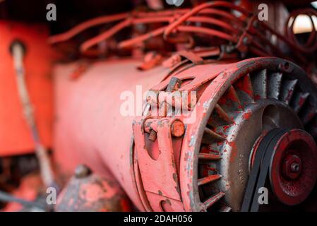 Primo piano del motore diesel a quattro cilindri con cinghia visibile cingoli arrugginiti parti idrauliche e cablaggio vernice rossa in sole giorno d'autunno Foto Stock