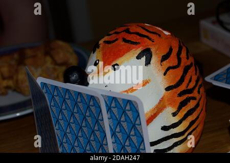 Un ornamento (o modello o giocattolo) di un riccio con le strisce arancioni e nere di una tigre, giocando un gioco di carte Foto Stock