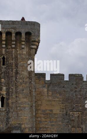 Una ragazza adolescente, con lunghi capelli brunette, si pone sulla cima dell'alta torre di pietra di un castello medievale europeo in rovina. Contro un cielo nuvoloso grigio. Foto Stock