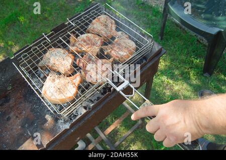 Primo piano di una mano dell'uomo che prepara carne fritta, all'aperto, in estate, sullo sfondo dell'erba Foto Stock