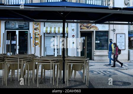 Lisbona, Portogallo. 10 Nov 2020. Una coppia che indossa maschere per il viso come misura preventiva cammina oltre i tavoli e le sedie accatastati in un ristorante. Credit: Jorge Castellanos/SOPA Images/ZUMA Wire/Alamy Live News Foto Stock