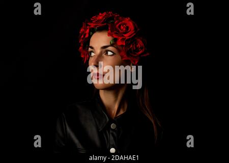 Giovane donna penosa in corona di fiori rossi su sfondo nero. Foto Stock