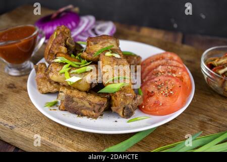 Costolette di maiale alla griglia su un osso servite su un piatto con verdure. Carne alla griglia arrosto su sfondo scuro. Foto Stock