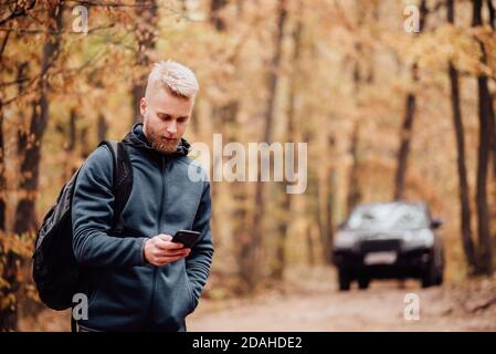 L'uomo viaggia in auto. Il ragazzo al telefono guarda dove si trova sul navigatore. Escursionista perso nel concetto di foresta d'autunno. Foto Stock