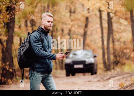 Il turista viaggia in auto. L'uomo al telefono guarda dove si trova sul navigatore. Il ragazzo si è perso nel concetto di foresta d'autunno. Foto Stock