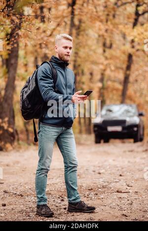 L'uomo viaggia in auto. Il ragazzo al telefono guarda dove si trova sul navigatore. Escursionista perso nel concetto di foresta d'autunno. Foto Stock