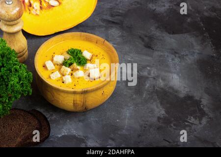 Zuppa di zucca con panna, pane e prezzemolo fresco in un piatto di metallo rustico su fondo nero grunge. Vista dall'alto, spazio di copia Foto Stock