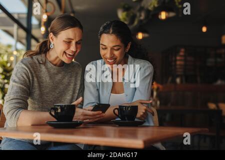 Amici che si divertono utilizzando uno smartphone al bar. Due donne che si siedono nel bar e sorridono. Foto Stock