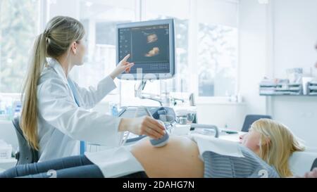 Nell'ospedale, l'ostetrista utilizza il trasduttore per la scansione ecografica dello screening del sonogramma ventaglio della donna incinta e punti il dito sullo schermo Foto Stock