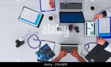 Vista dall'alto dei medici residenti che consigliano con il medico utilizzando una videocall seduto sulla scrivania in clinica con attrezzatura medica. Parlare con uno specialista di videoconferenza on-line su copy space, flat lay Foto Stock