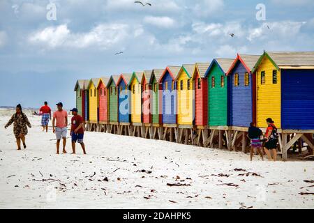 Muizenberg, Città del Capo, Sudafricana - 31 DICEMBRE 2017: Persone che camminano di fronte a iconiche cabine colorate sulla spiaggia contro il cielo nuvoloso Foto Stock