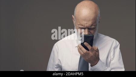Uomo di mezza età che ha difficoltà e problemi di visione utilizzando il suo smartphone, non è in grado di leggere piccoli testi sullo schermo Foto Stock