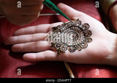 Primo piano macro shot di tatuaggio henné mehendi applicato in un modello intricato sulla mano di una donna con luce naturale soffusa e su un rosso Foto Stock