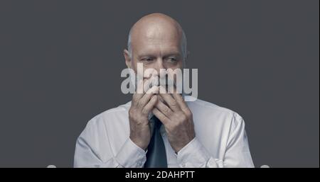 Uomo d'affari di mezza età confuso pensando e guardando via, sta tenendo il mento e si sente sospettoso Foto Stock
