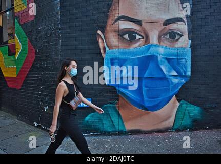 GRAN BRETAGNA / Inghilterra / Londra /UNA donna con maschera facciale cammina oltre un pezzo di Street art raffigurante un infermiere NHS indossando una maschera facciale su 22,04. 2020. Foto Stock