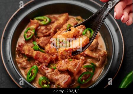Bicol Express Stew in ciotola nera su tavolo di ardesia scuro. Cucina filippina piccante pancia di maiale cocco latte curry. Cibo asiatico. Foto Stock