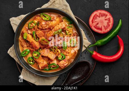 Bicol Express Stew in ciotola nera su tavolo di ardesia scuro. Cucina filippina piccante pancia di maiale cocco latte curry. Cibo asiatico. Vista dall'alto Foto Stock