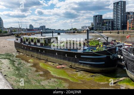 Grandi chiatte olandesi convertite in barche di casa ora sedersi sul fango al loro ormeggi a bassa marea sul fiume Tamigi a Battersea. Foto Stock