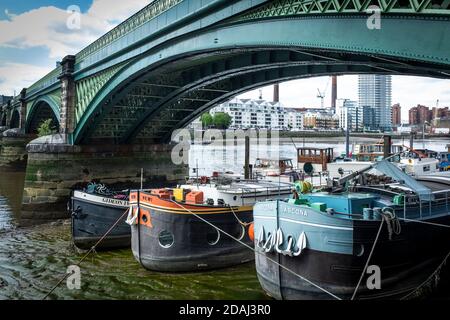 Le chiatte convertite in barche, siedono sul fiume Tamigi con la bassa marea sotto il Ponte ferroviario di Battersea (originariamente chiamato il Ponte di Cremorne Foto Stock