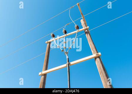 Polo elettrico in legno con fili elettrici ad alta tensione contro cielo blu Foto Stock