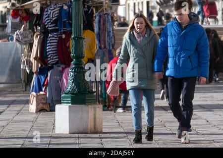 Una giovane coppia cammina lungo un negozio di abbigliamento sul lungomare centrale di Riva degli Schiavoni in una giornata di sole invernale. Foto Stock