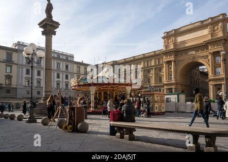 La gente cammina in Piazza della Repubblica (ital. Piazza della Repubblica) con una giostra per bambini, l'arco di Vittorio Emanuele II e una colonna di abbondanza Foto Stock