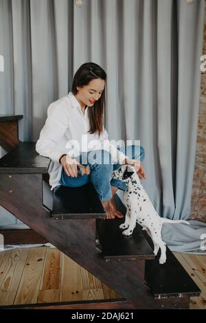 Giovane donna si siede sulla scala e gioca con il cucciolo del cane dalmata. Foto Stock