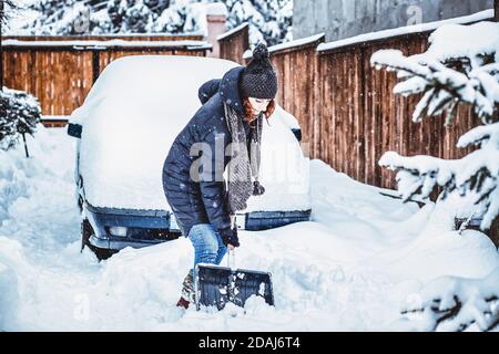 donna con pala che pulisce la neve intorno all'auto. Pala invernale. Rimuovere la neve dopo la bizzarda Foto Stock