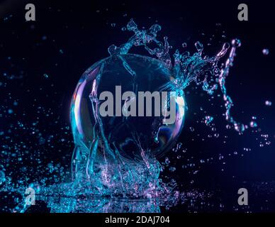 acqua blu e viola che spruzzi su una palla trasparente dentro uno sfondo scuro Foto Stock