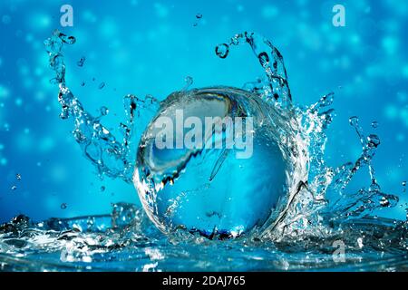 onda d'acqua che spruzzi su una palla trasparente in un blu sfondo Foto Stock