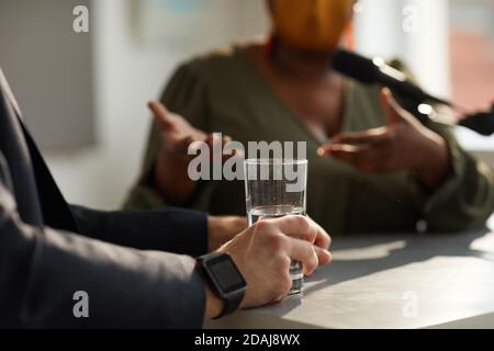 Primo piano di un uomo seduto al tavolo con un bicchiere di water durante il colloquio di affari con la donna Foto Stock